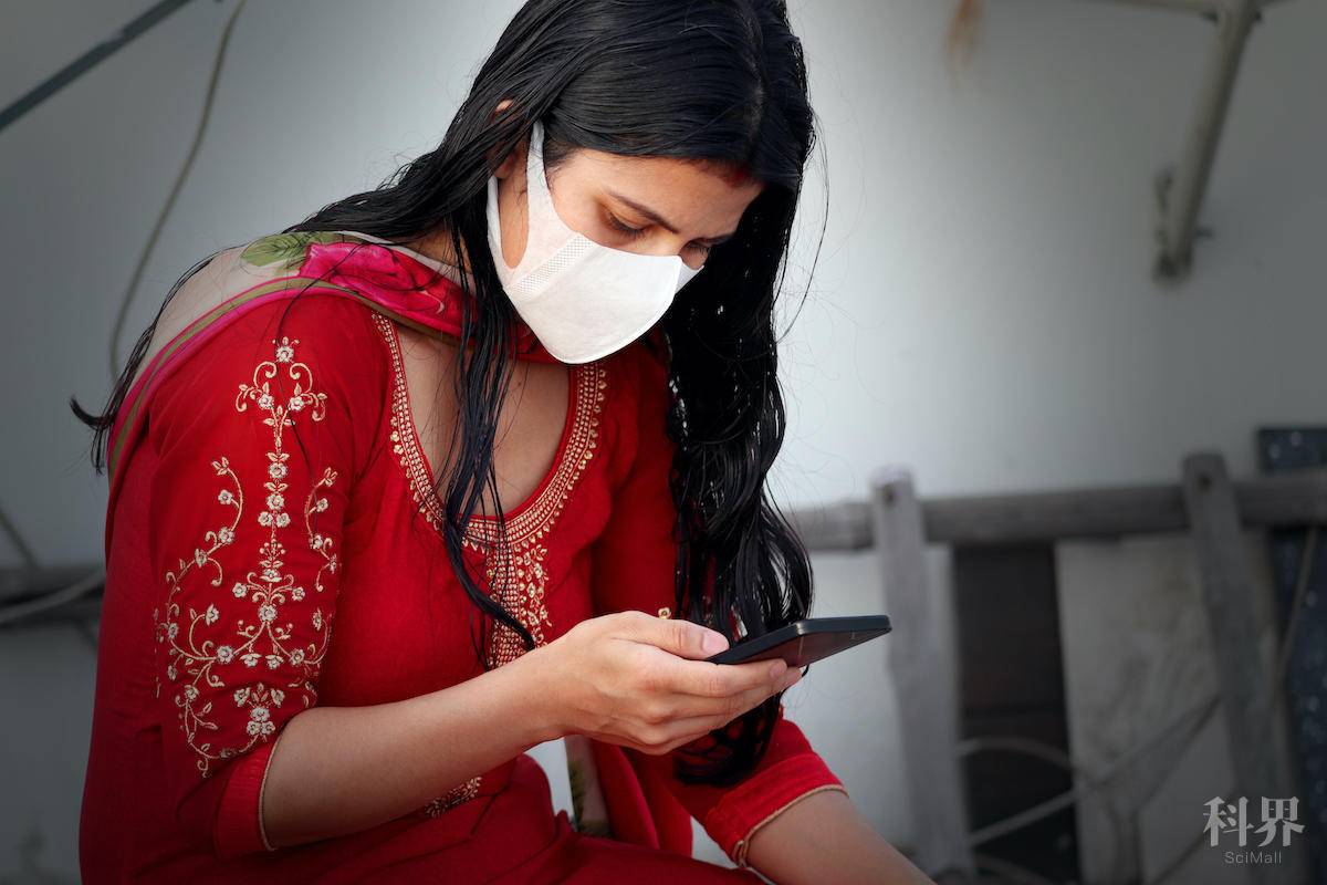 Young Indian women wearing pollution mask against Coronavirus or COVID-19 and she using mobile phone at home.